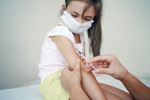 girl wearing a facemaks and receiving a vaccine on her arm