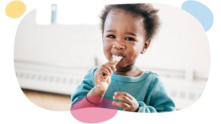toddler sticking spoon with yogurt into his mouth.