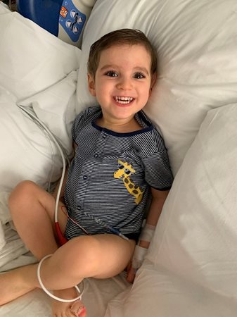 Matthew  on his hospital bed smiling and wearing a blue top with a giraffe on it.