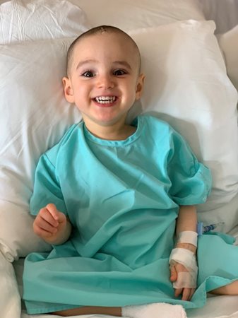 Matthew wearing a hospital gown on his bed smiling.