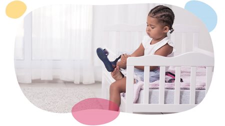 girl putting on her strap on sandals while sitting on bed.