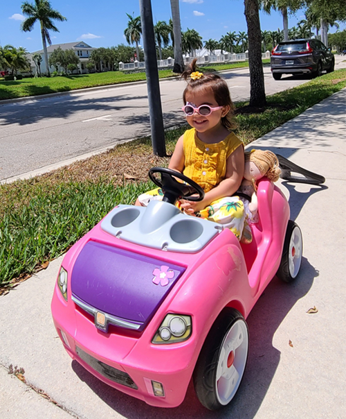 Bruna, riding an electric toy car.